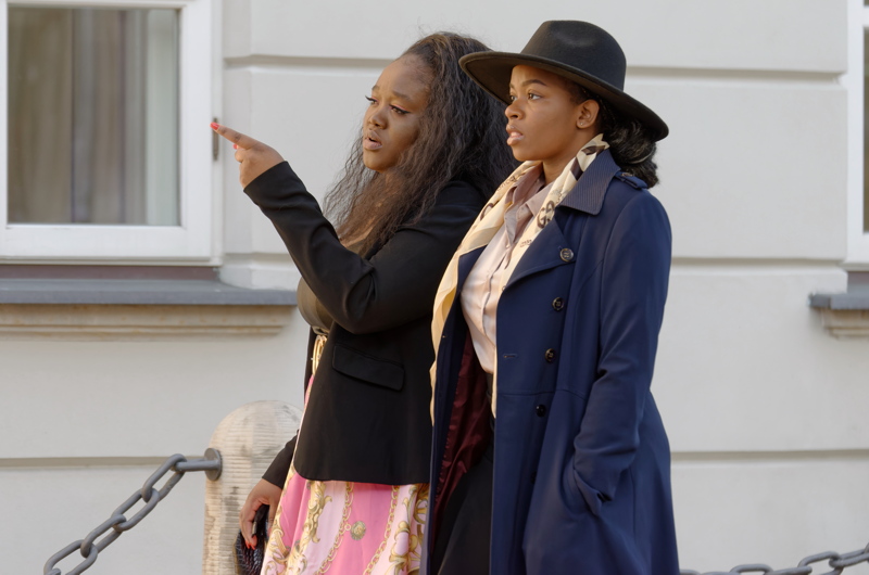 23 - Two individuals in street fashion, with the person on the right wearing a navy blue trench coat and a black fedora hat
